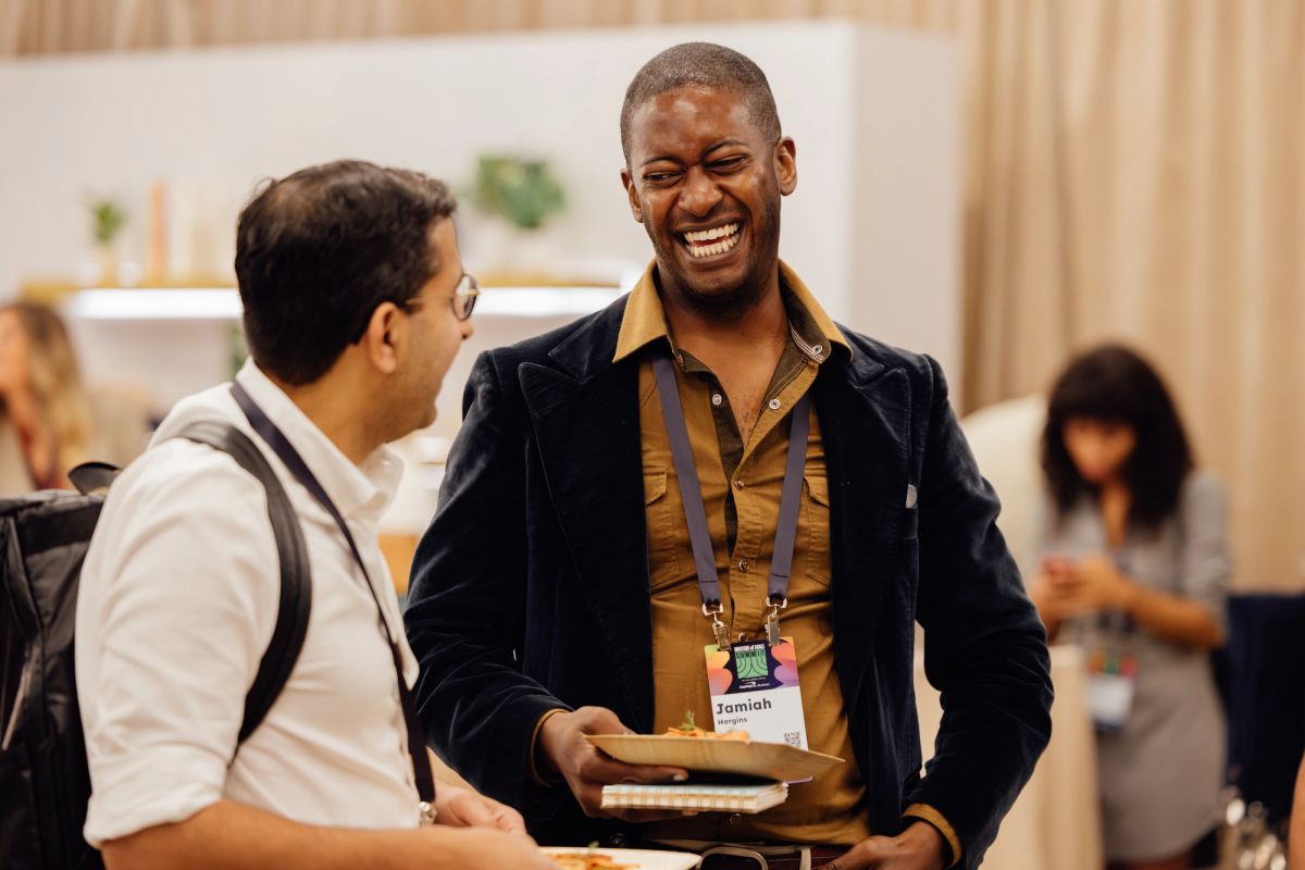 Two conference attendees networking and smiling, one wearing a name badge, in an indoor event space.