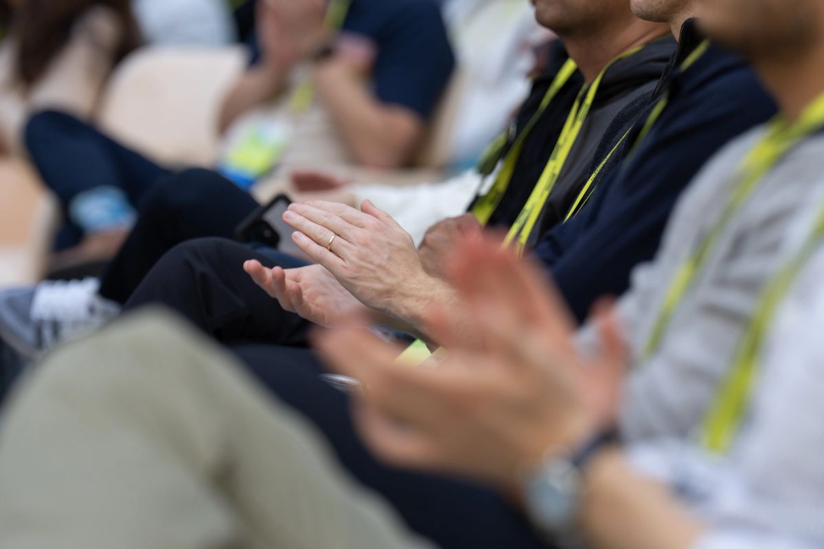 Seated conference attendees wearing lanyards clapping during a session.