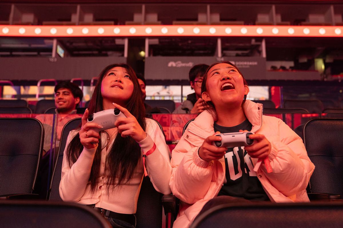 Two attendees playing video games with controllers while seated in arena-style venue with red lighting