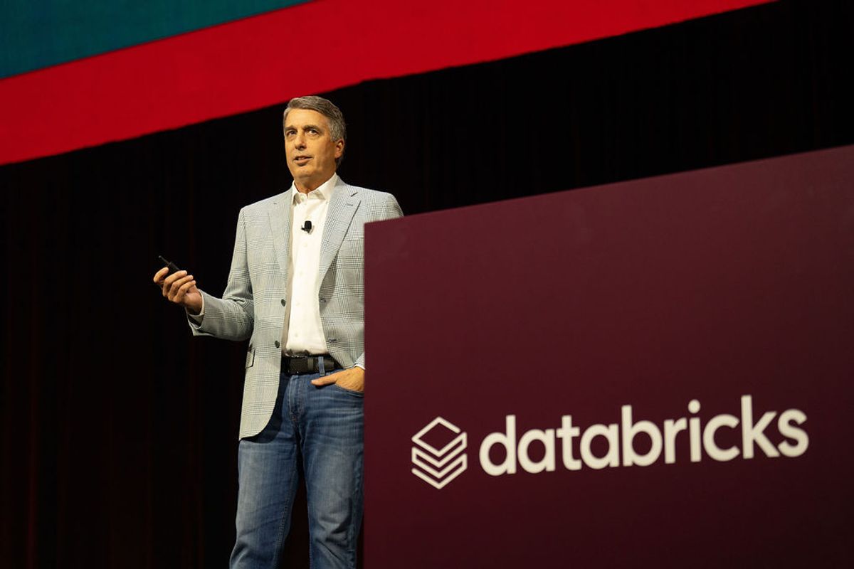 Executive presenting on stage with Databricks logo backdrop at conference venue