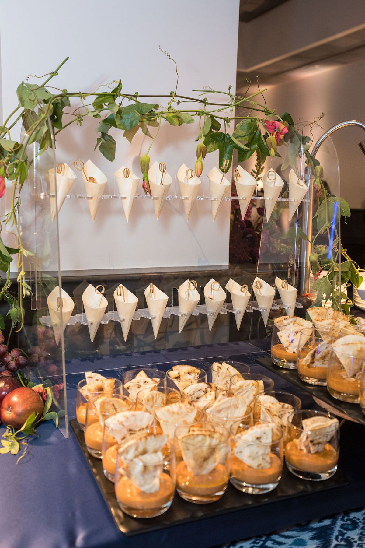 Elegant appetizer display with small glasses containing layered desserts and paper cone holders arranged on.