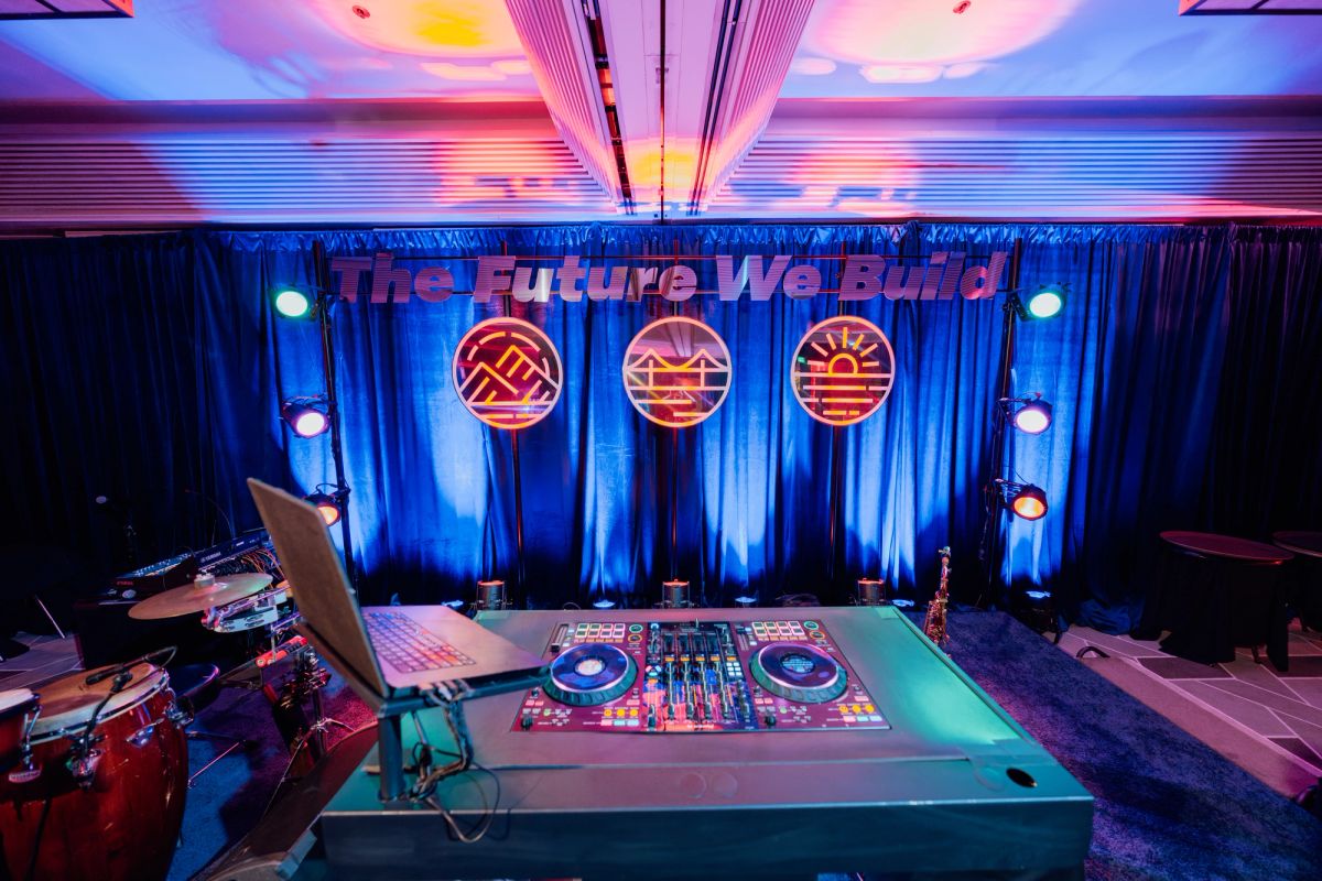 DJ setup with turntables and mixer on stage with blue backdrop featuring three circular neon signs and "The.