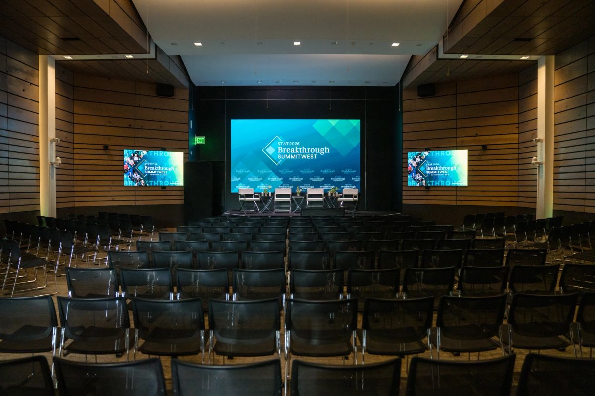 Auditorium with rows of empty black chairs facing a stage with large screens displaying "Breakthrough Summit.