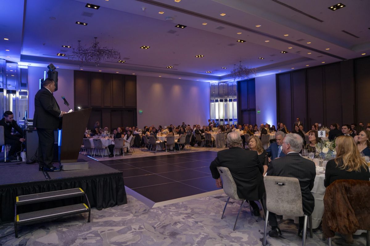 Speaker at podium addressing seated audience in elegant hotel ballroom with blue accent lighting