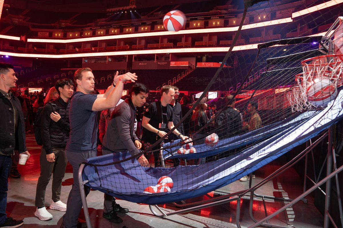 Conference attendees playing a basketball shooting game at an arena event with red lighting