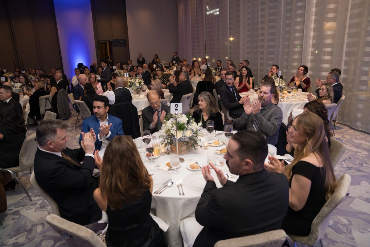 Formally dressed attendees applauding at round tables during an elegant gala dinner event in a ballroom