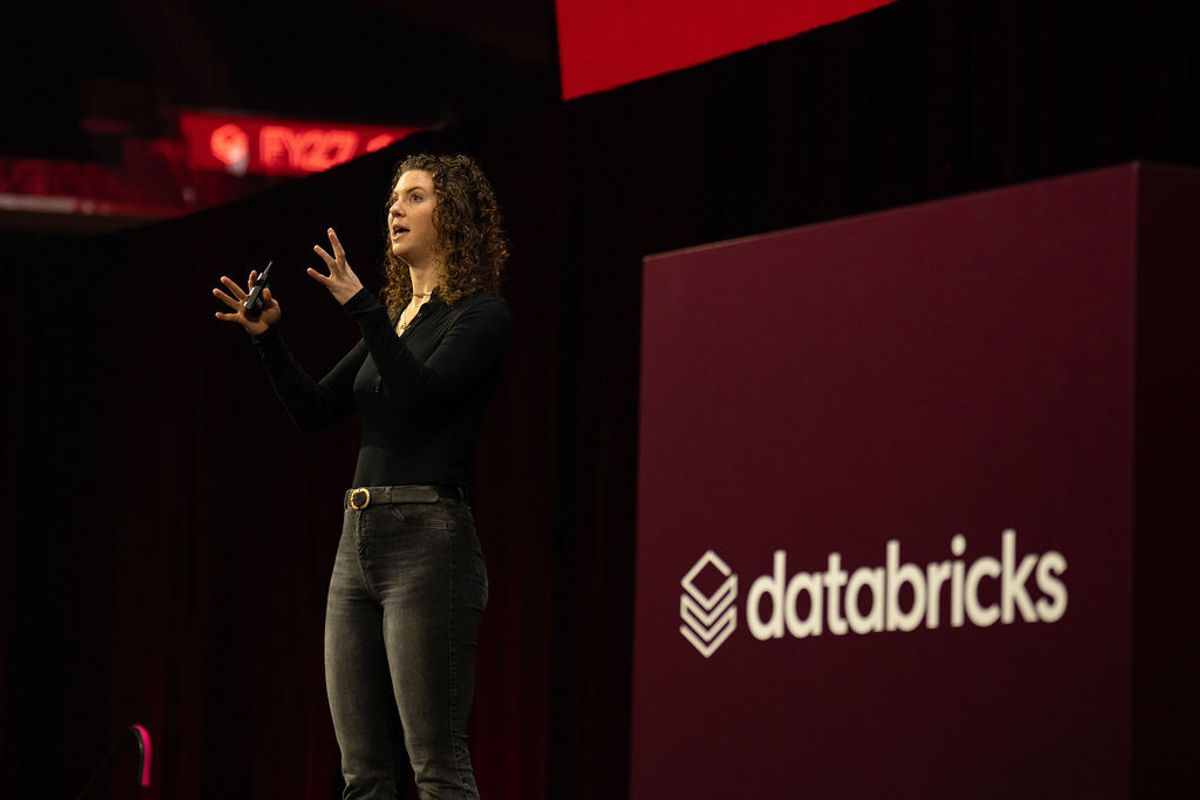 Speaker presenting on stage at Databricks conference with red and black backdrop