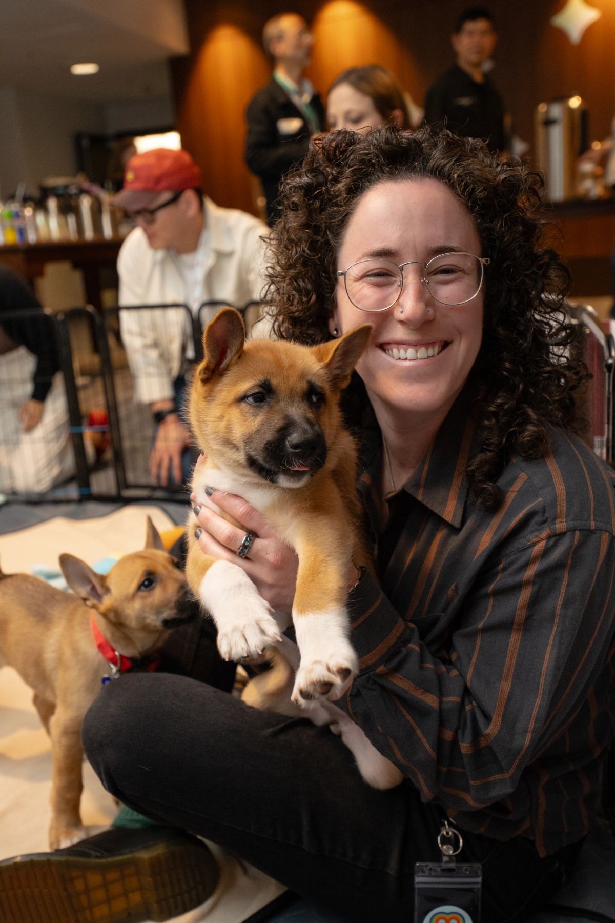 Attendee holding a tan puppy and smiling at a conference, another puppy visible nearby.