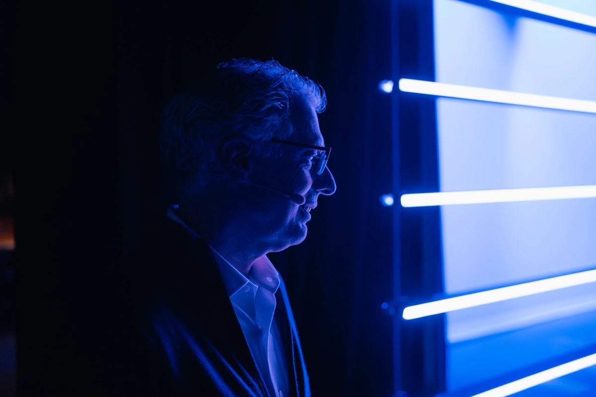 Speaker in profile illuminated by blue stage lighting at conference venue