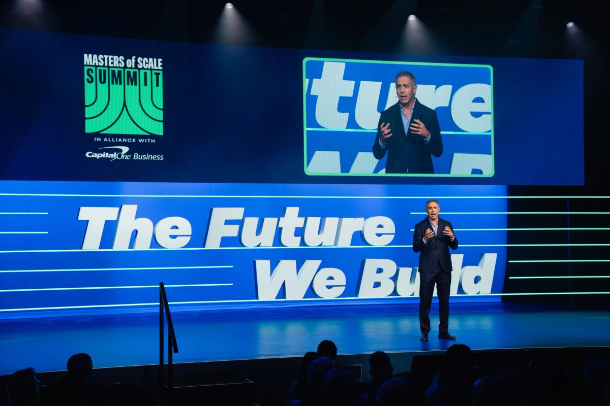 Speaker presenting on stage with "The Future We Build" backdrop and "Masters of Scale Summit" branding visible