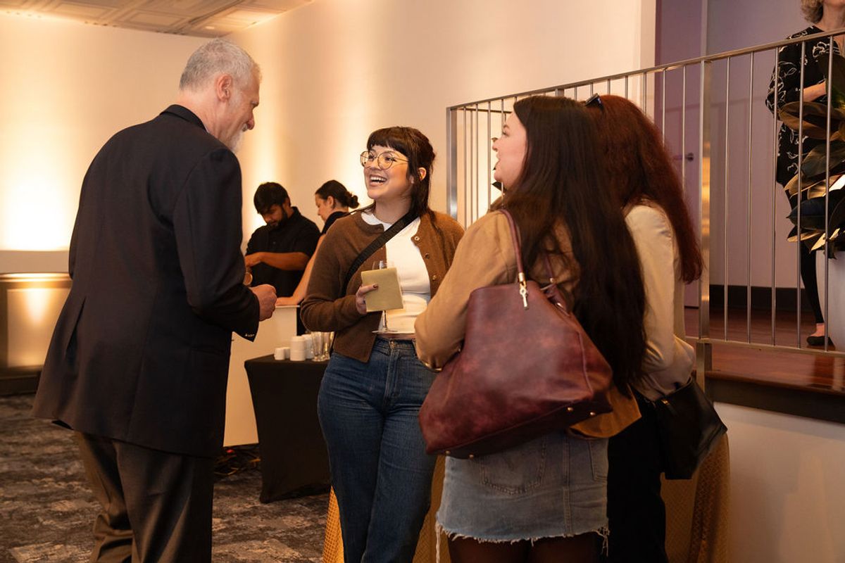 Man in suit networking with two women at indoor reception event with modern venue lighting