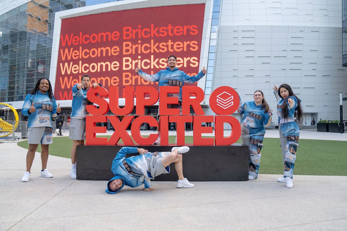 Group of attendees posing playfully around large red "SUPER EXCITED" sign with "Welcome Bricksters" backdrop