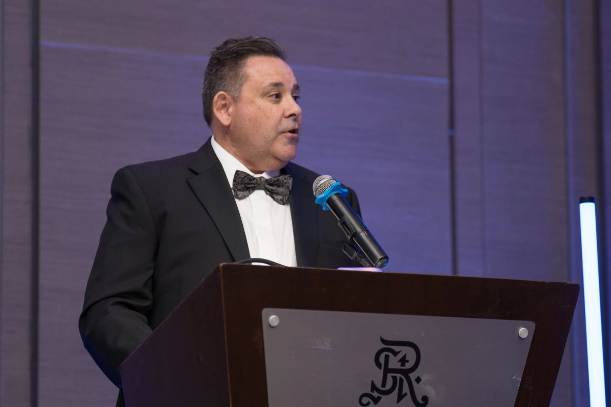 Speaker in tuxedo delivering remarks at podium during formal gala event