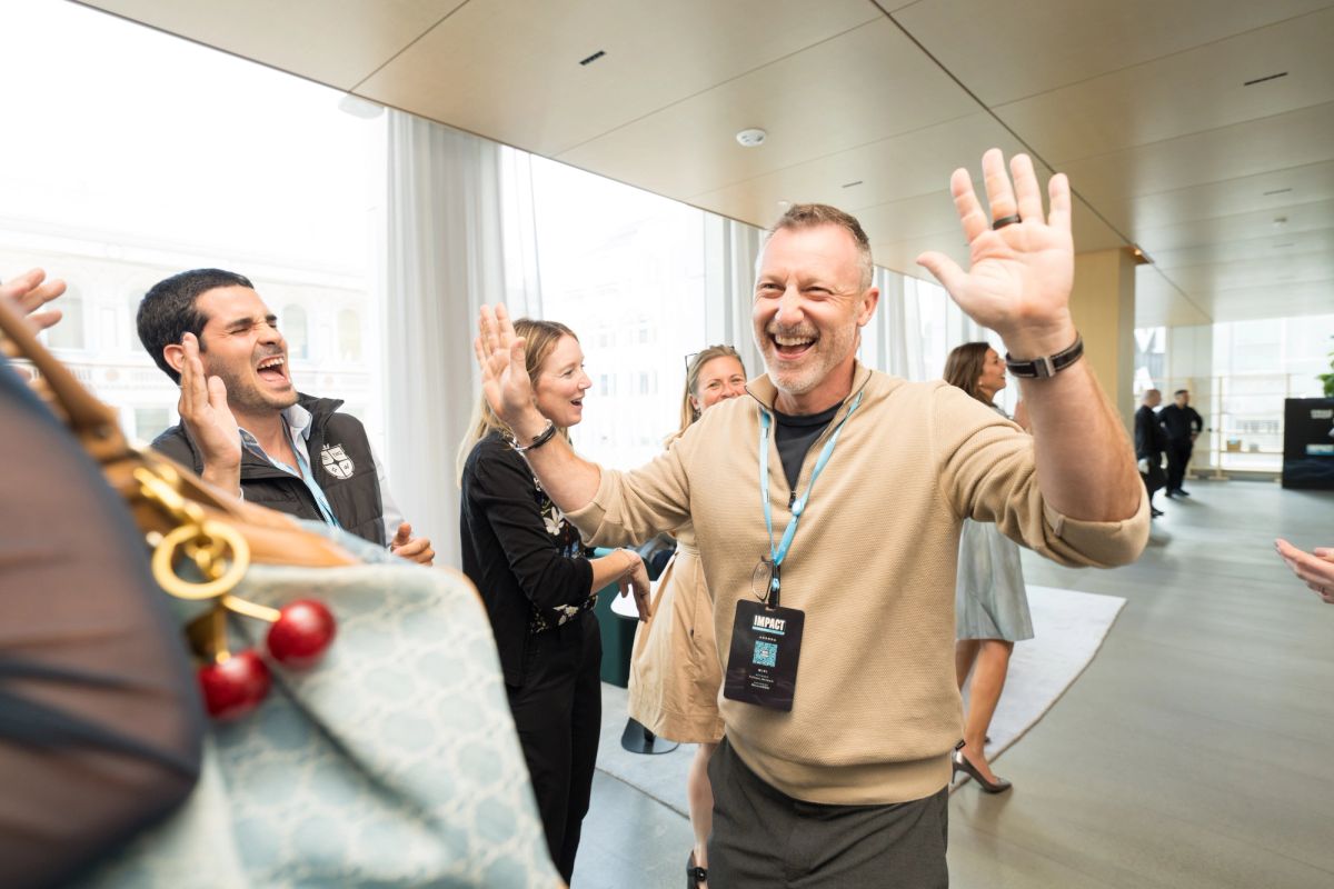 Conference attendees celebrating with raised hands and smiles in modern venue lobby with large windows