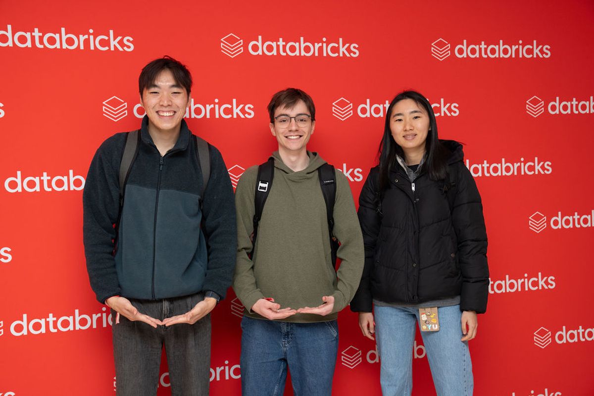 Three attendees pose together in front of a red Databricks backdrop wall at a conference event.