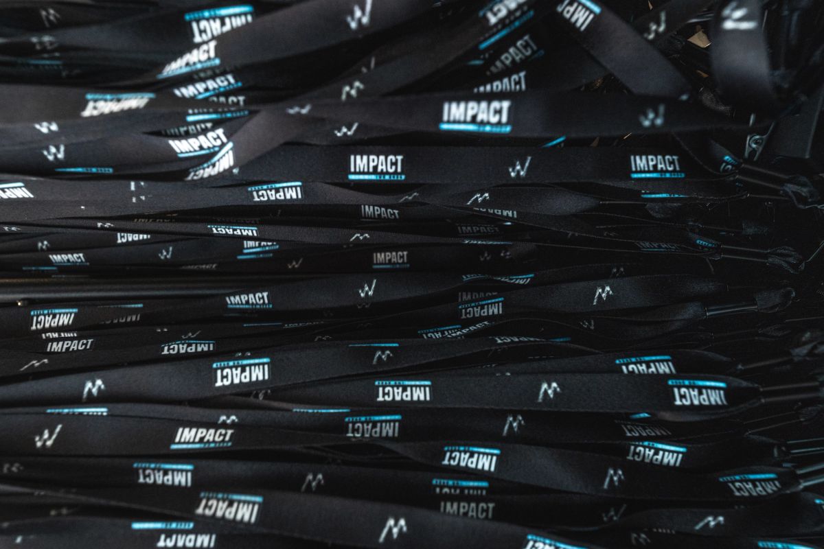 Black branded lanyards with the word IMPACT text scattered across a dark surface at a conference event.