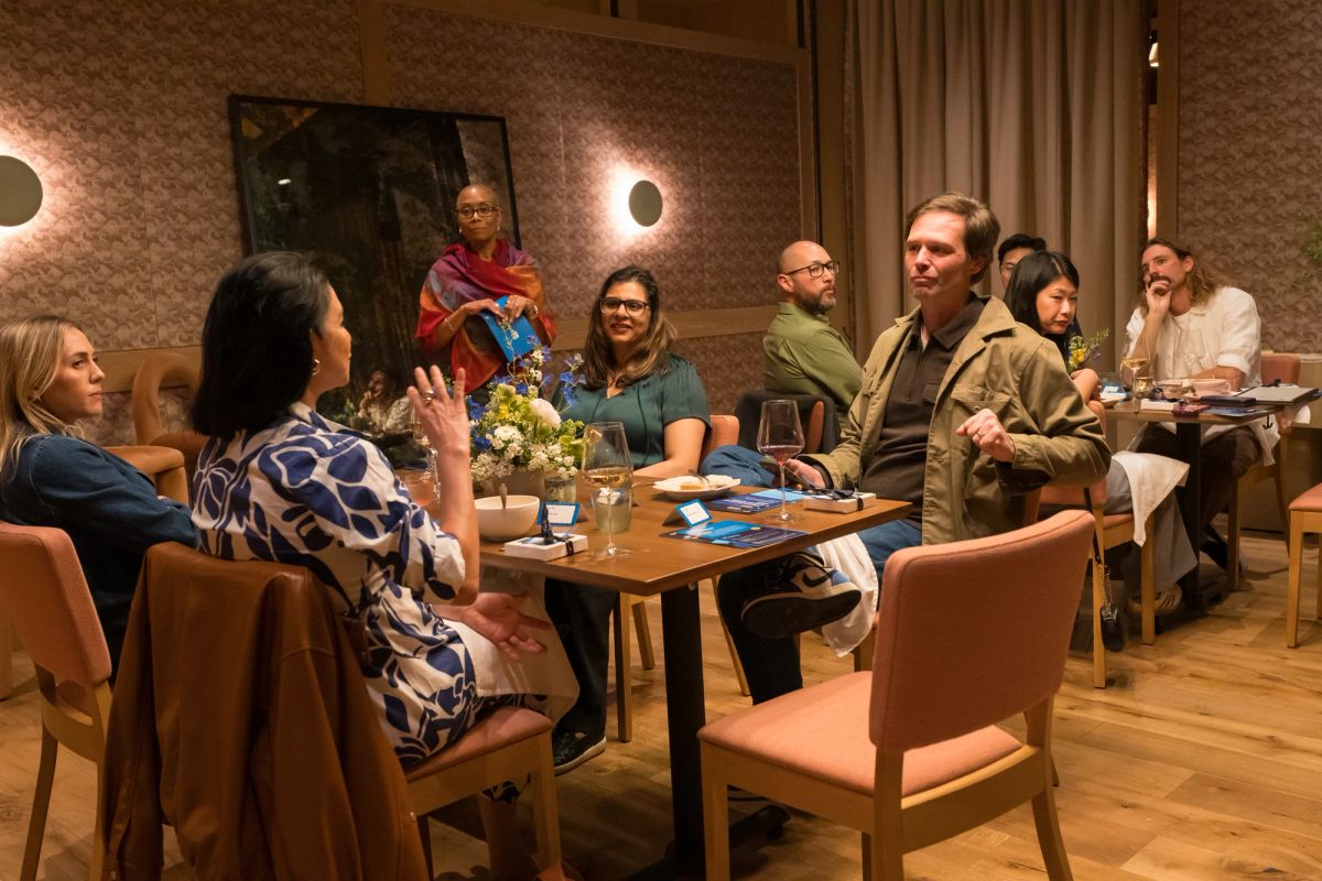 Panel discussion with speakers and audience seated around tables in modern restaurant setting