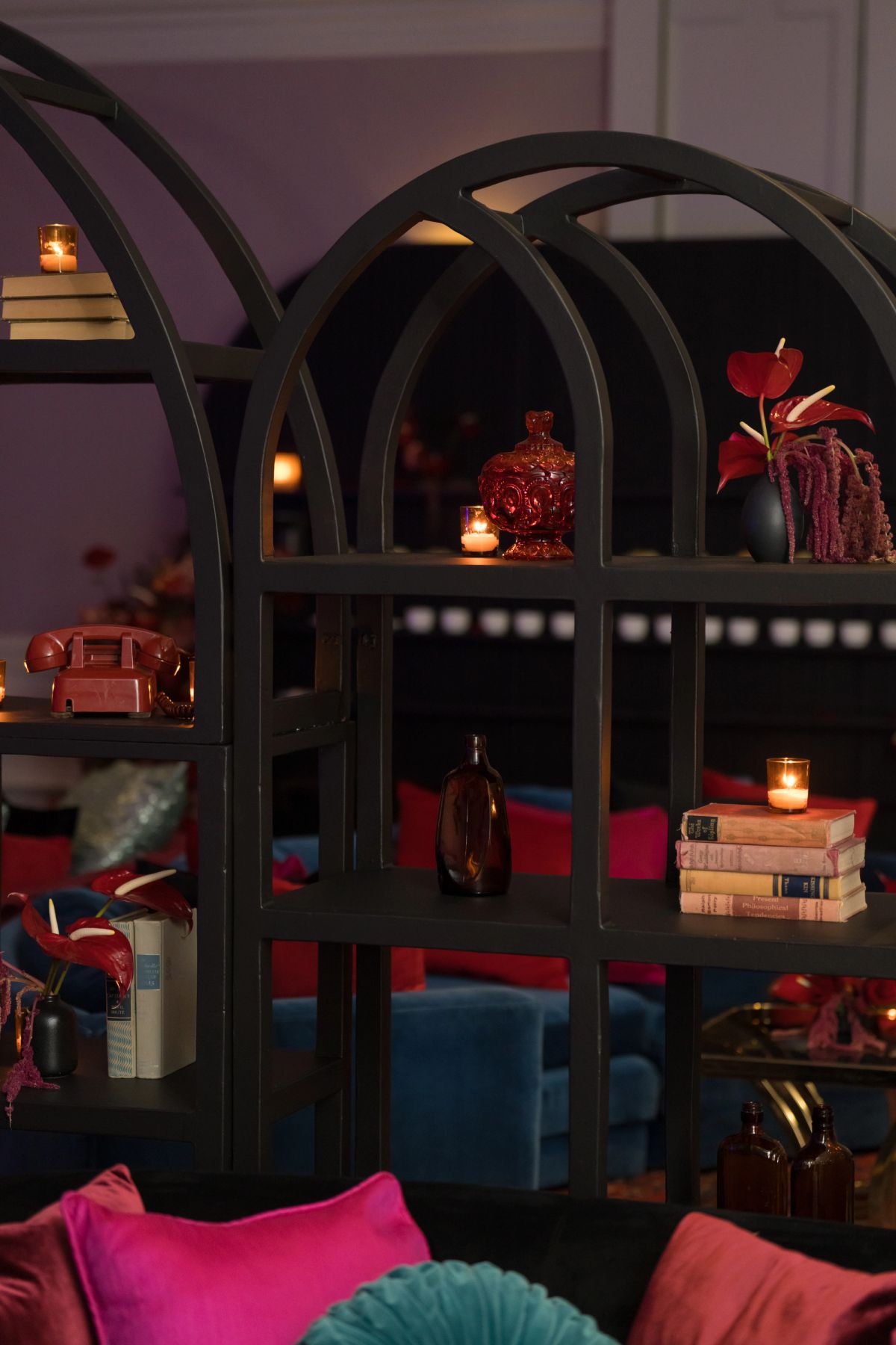 Dark shelving unit with arched design displaying books, candles, decorative objects and red flowers in cozy.