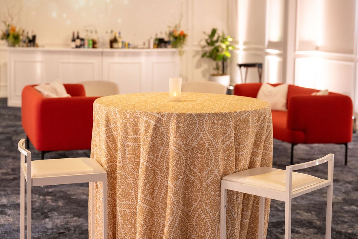 Round table with golden tablecloth and wooden chairs in elegant reception space with red seating area