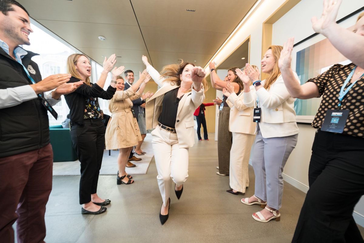 Conference attendees celebrating with raised hands and applause in a modern office hallway