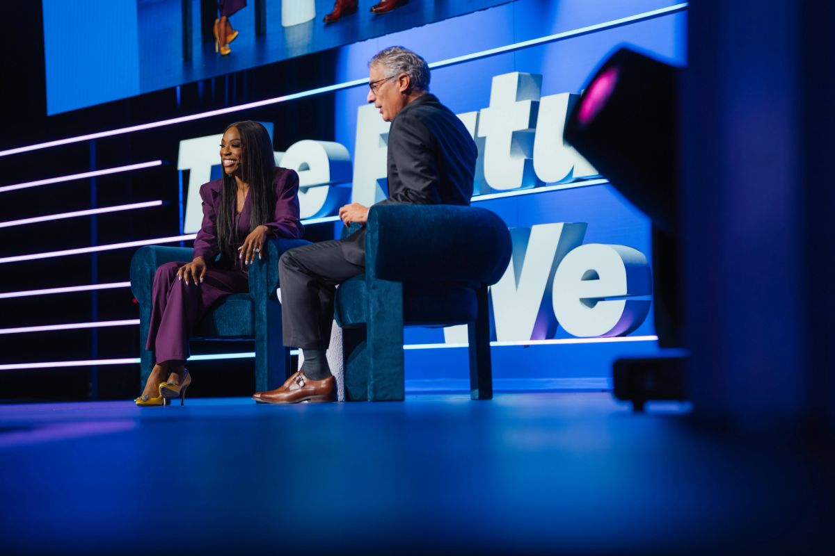 Two speakers sitting on blue chairs during conference presentation on illuminated stage with blue lighting