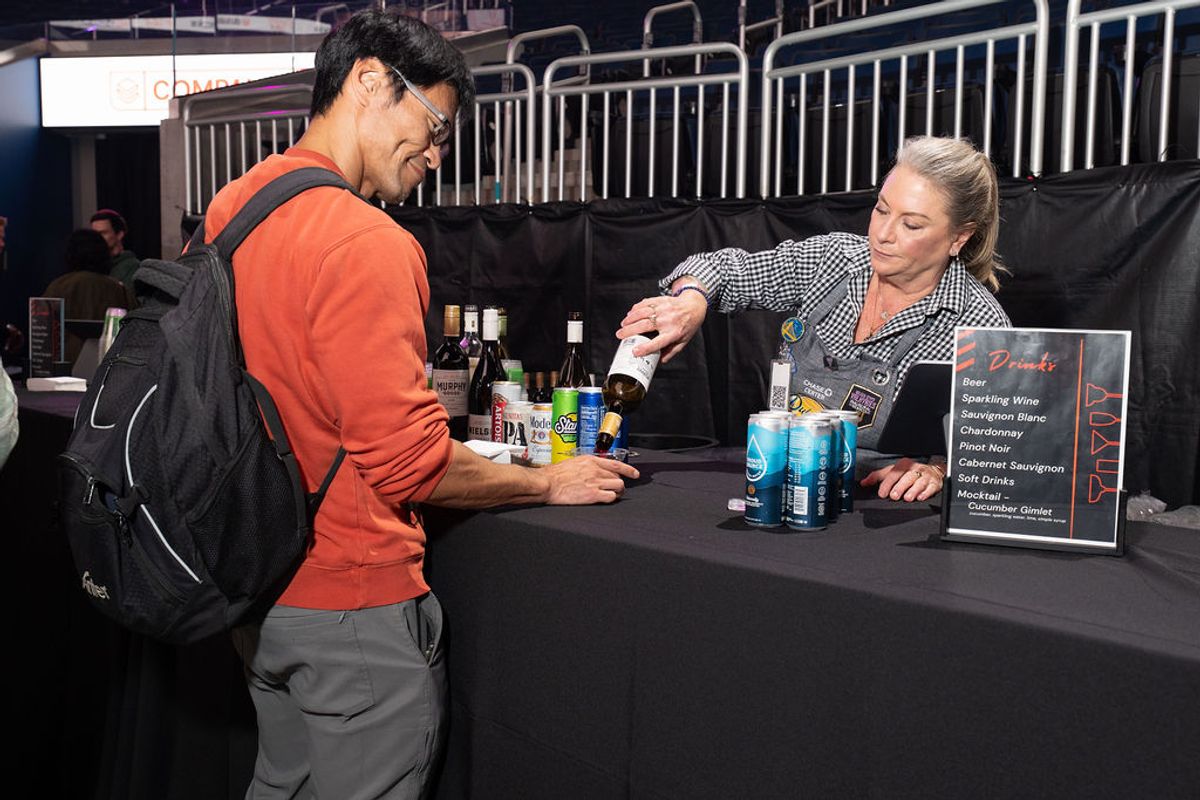 Attendee receives drink from bartender at conference networking event with wine menu visible on table