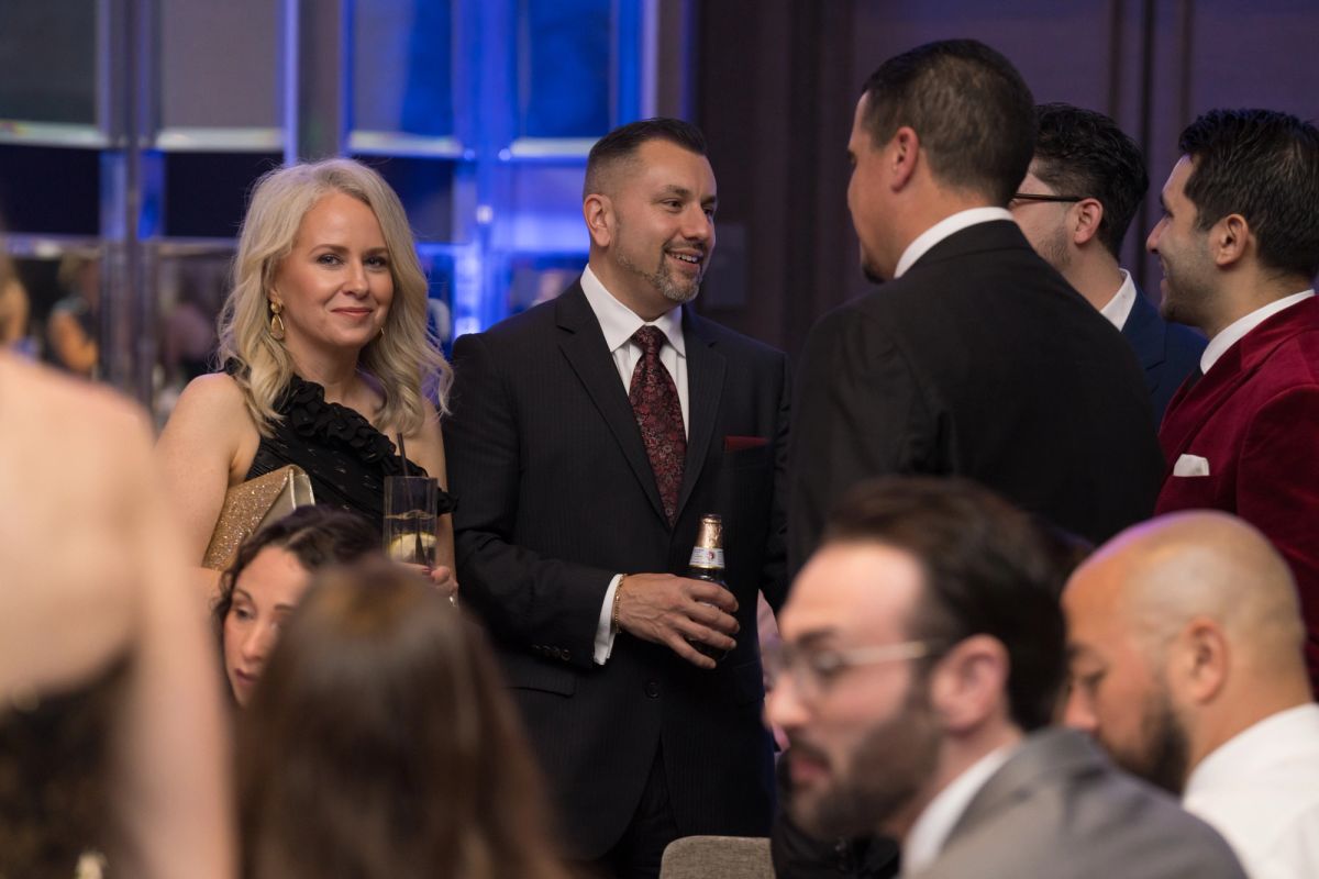 Formally dressed attendees networking and socializing at an upscale evening event with blue lighting.
