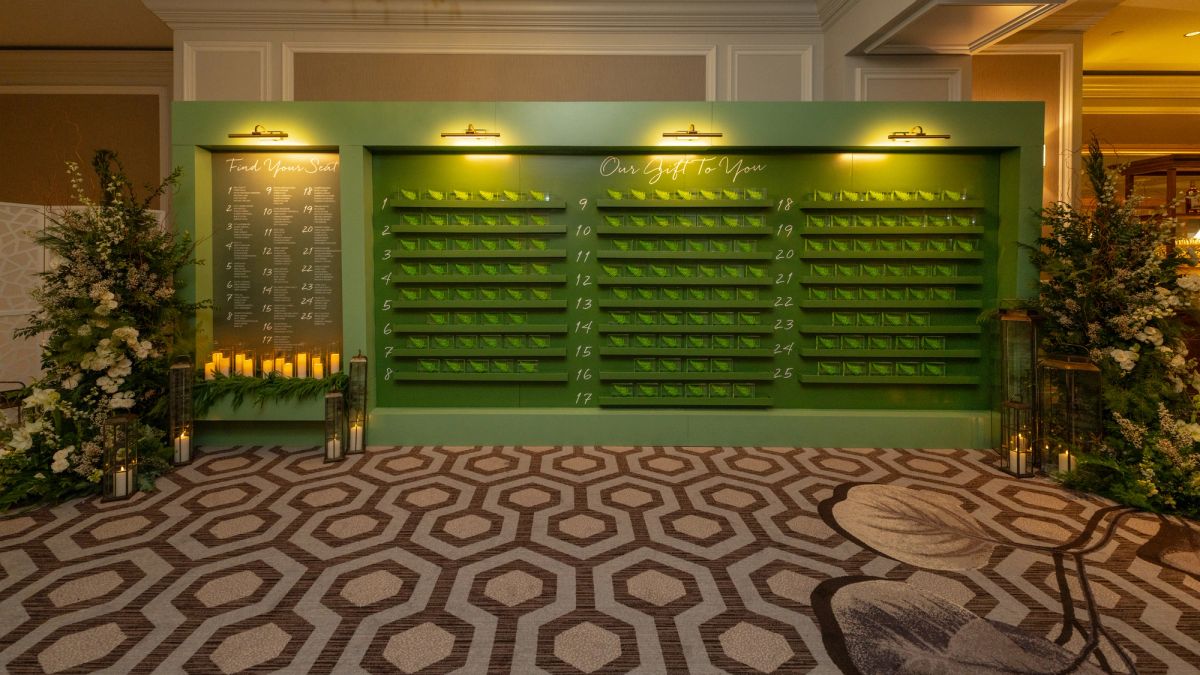 Green display wall with multiple shelves flanked by floral arrangements in elegant hotel lobby with patterned.