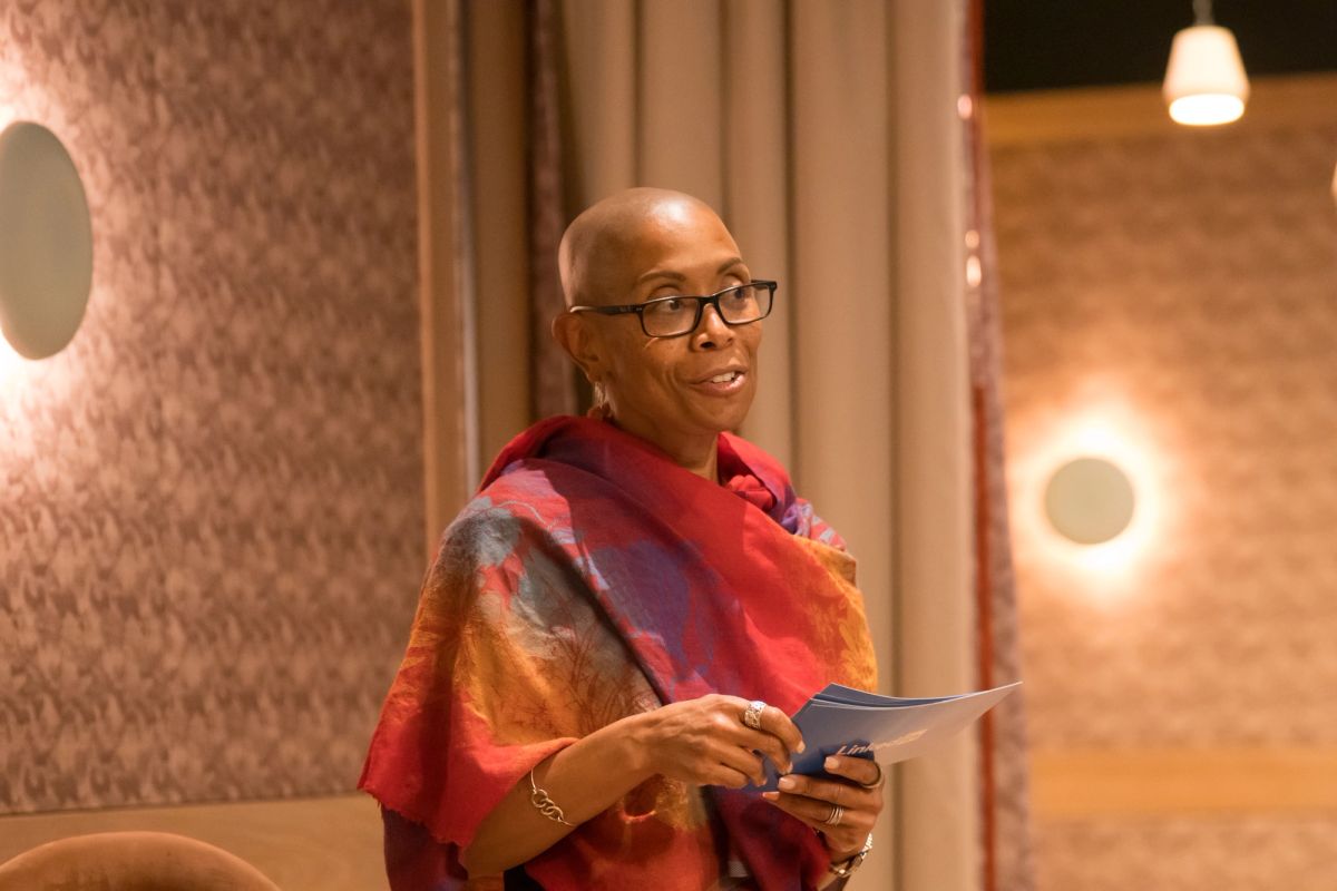Panelist in colorful shawl holds papers during panel discussion in modern venue with warm lighting