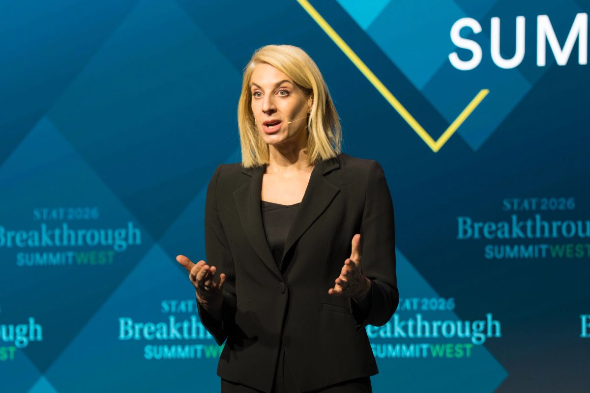 Speaker presenting at Breakthrough Summit event with blue backdrop and geometric design elements
