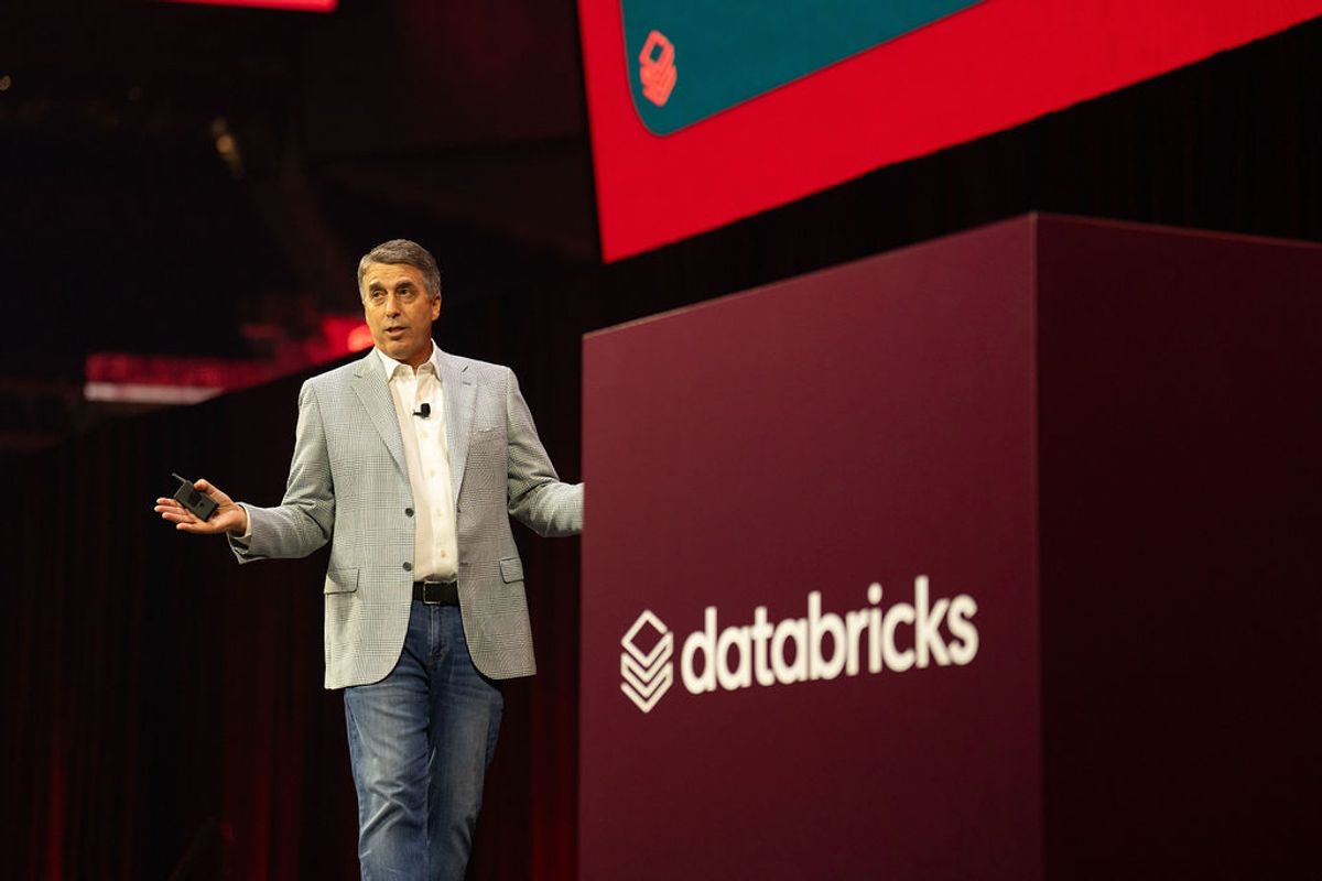 Executive presenting on stage at Databricks conference with red and burgundy branded backdrop