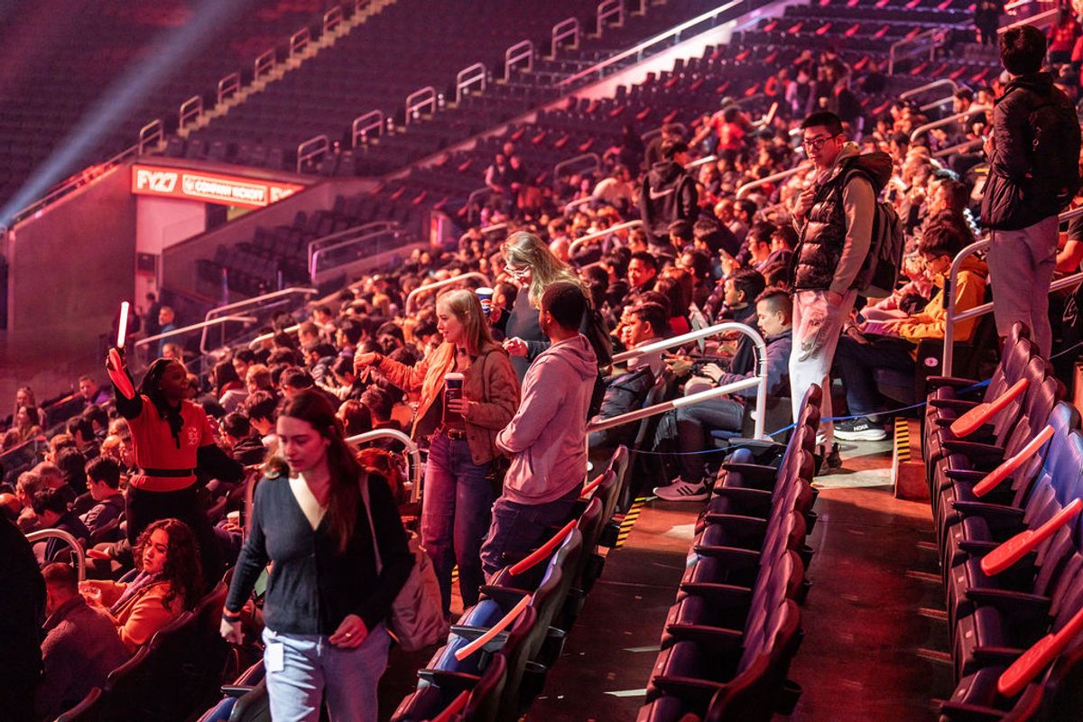 Attendees standing and applauding in arena seating during an event with red stage lighting