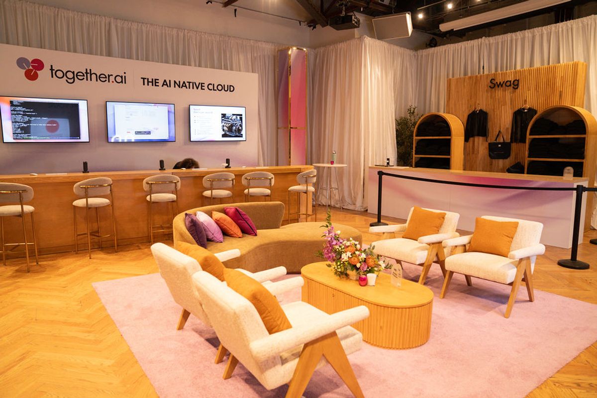Modern conference booth with white lounge seating, orange accents, bar stools, and displays showing.