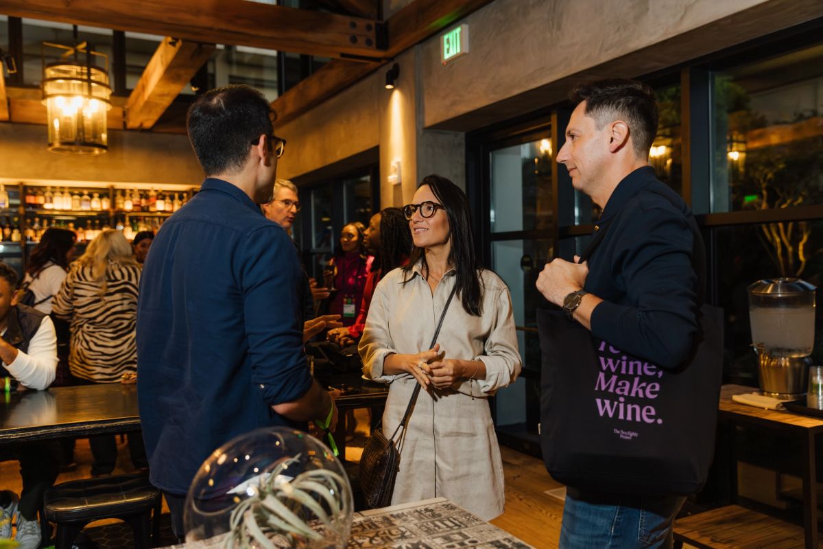 Three people networking and conversing in a modern restaurant or bar setting with warm lighting and exposed.