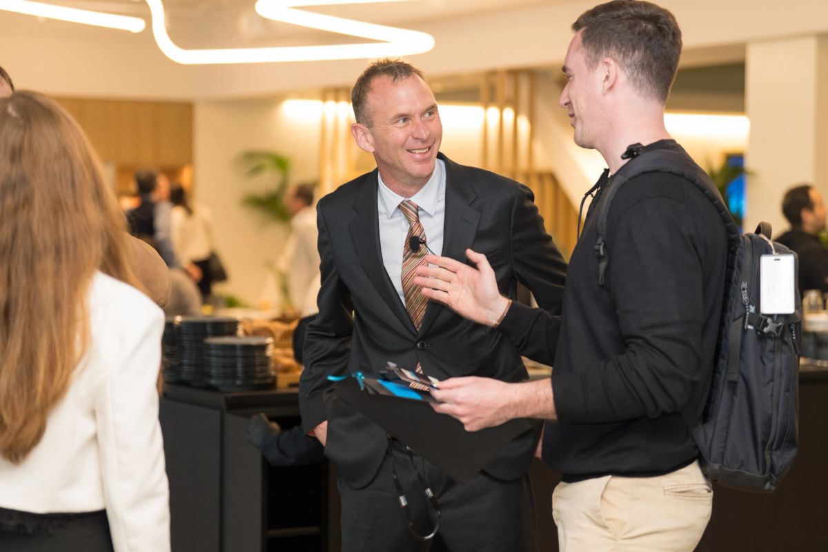 Two men in business attire networking and conversing at a conference event in a modern venue lobby.