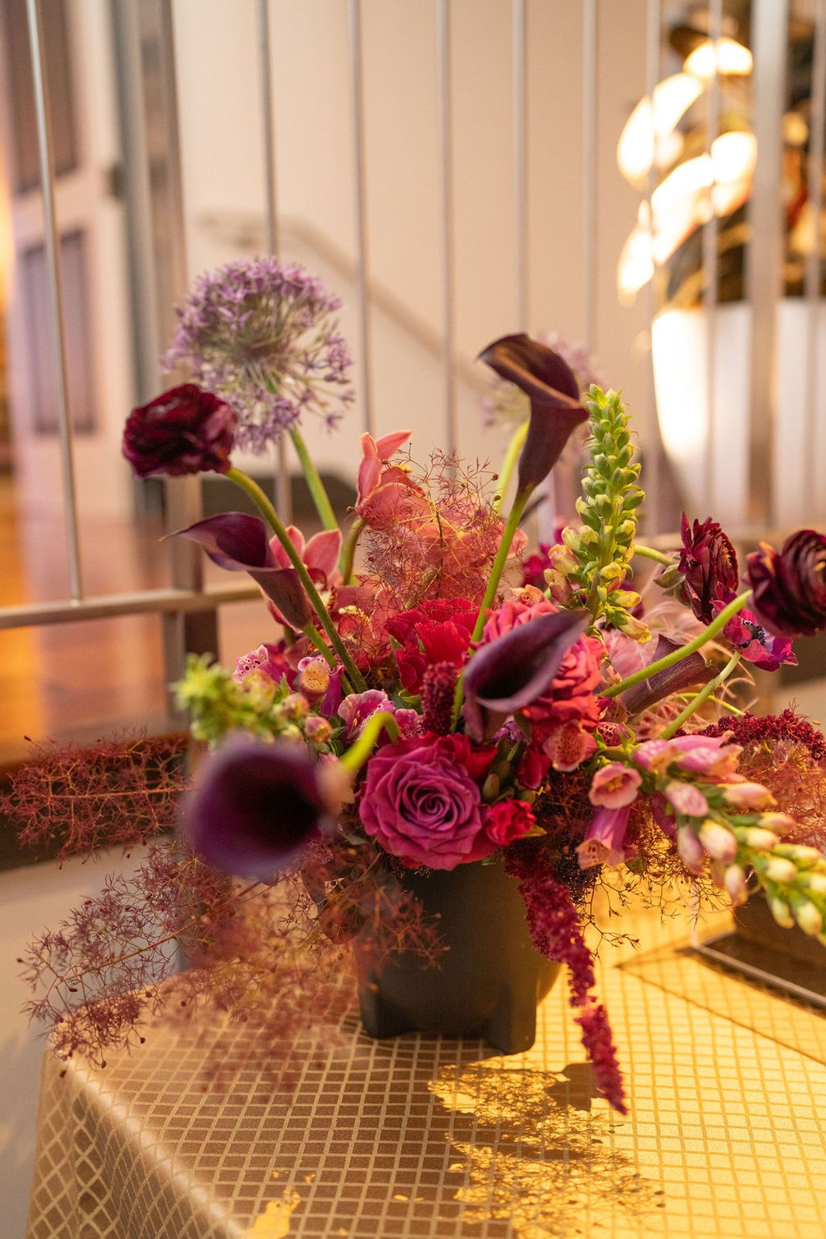 Elegant floral arrangement with purple roses and calla lilies on tiled surface with warm lighting in.