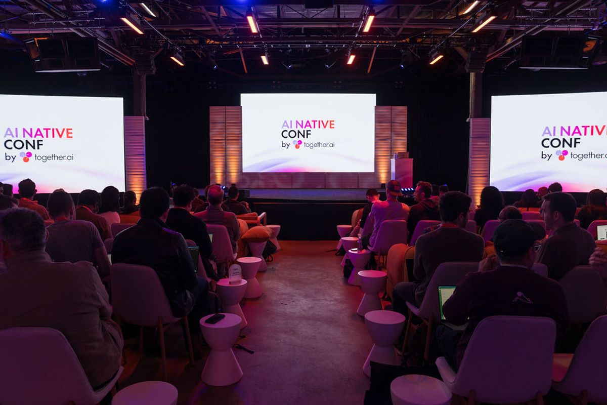 Audience seated in auditorium facing stage with AI Native Conf presentation screen and colorful lighting
