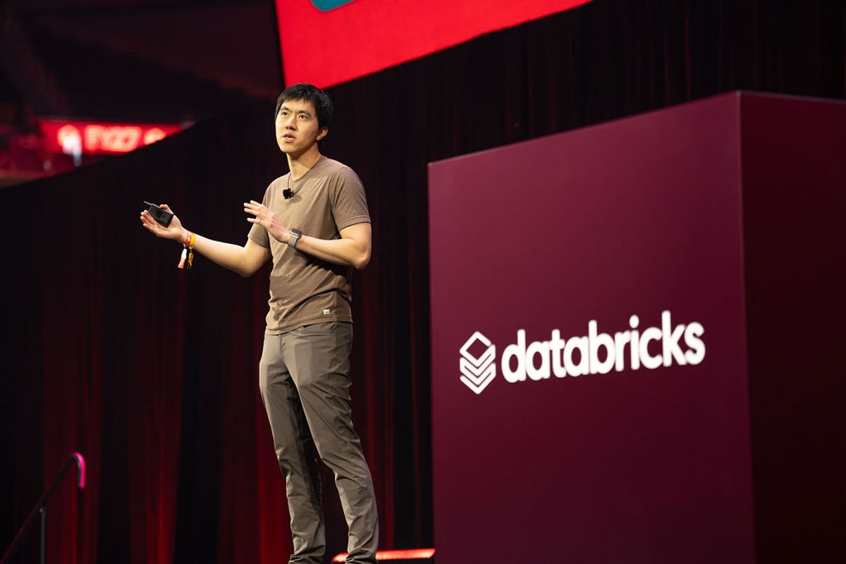 Speaker presenting on stage with Databricks branding backdrop at conference venue