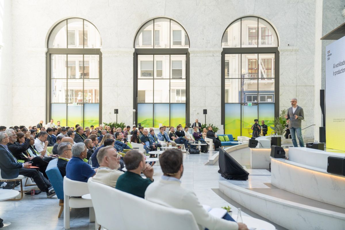 Speaker presenting to seated audience in elegant marble hall with arched windows.