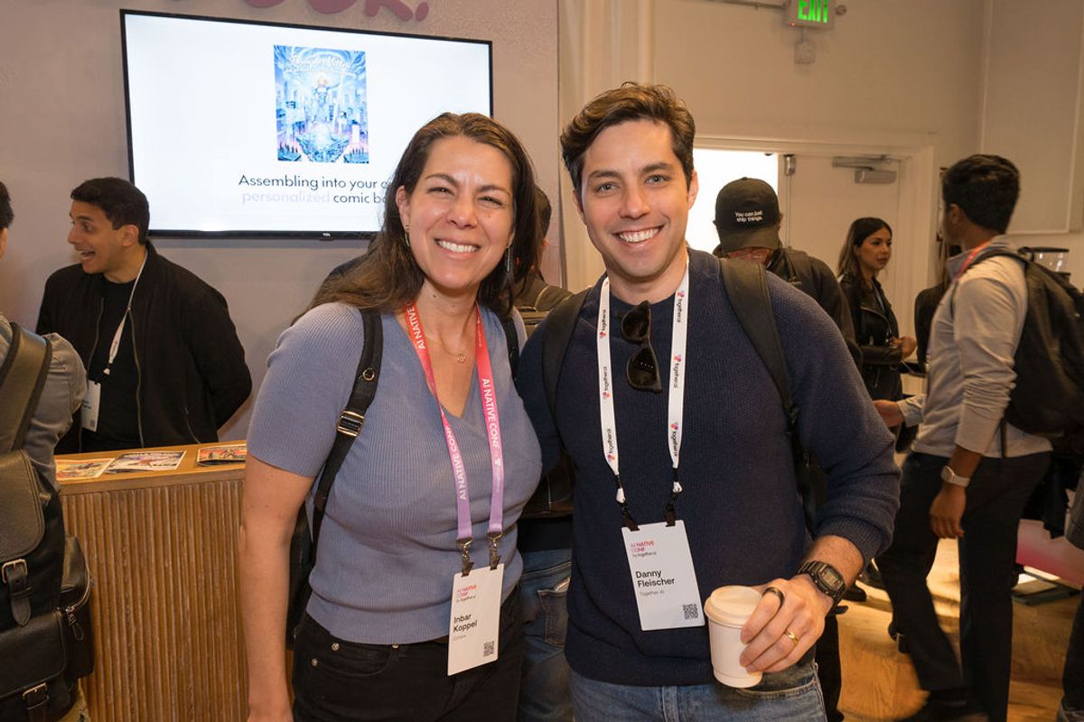 Two conference attendees with name badges smile together at a networking event with presentation screen in.