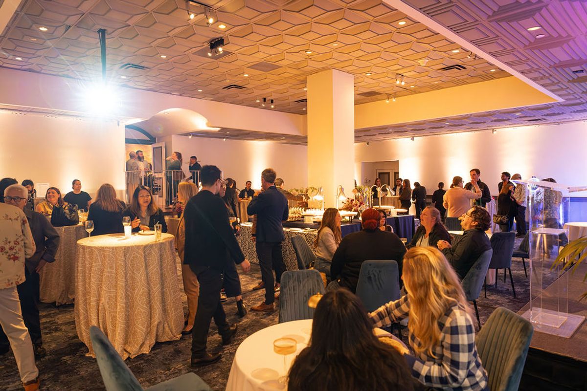 Networking reception with attendees mingling around cocktail tables in an elegant event space with warm.