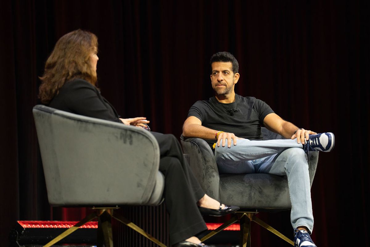 Two people having an on-stage interview at a conference, sitting in modern chairs with dark backdrop