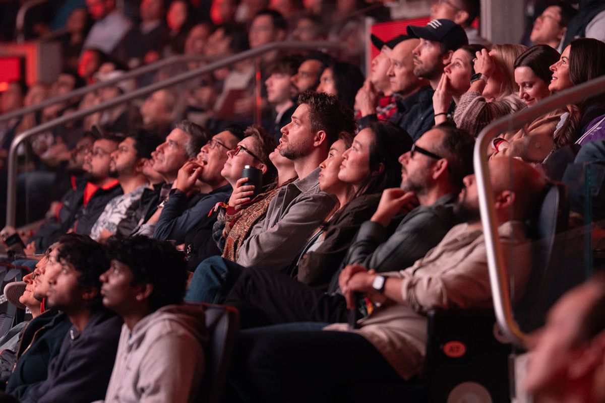 Audience members seated in tiered seating looking up attentively during a conference presentation