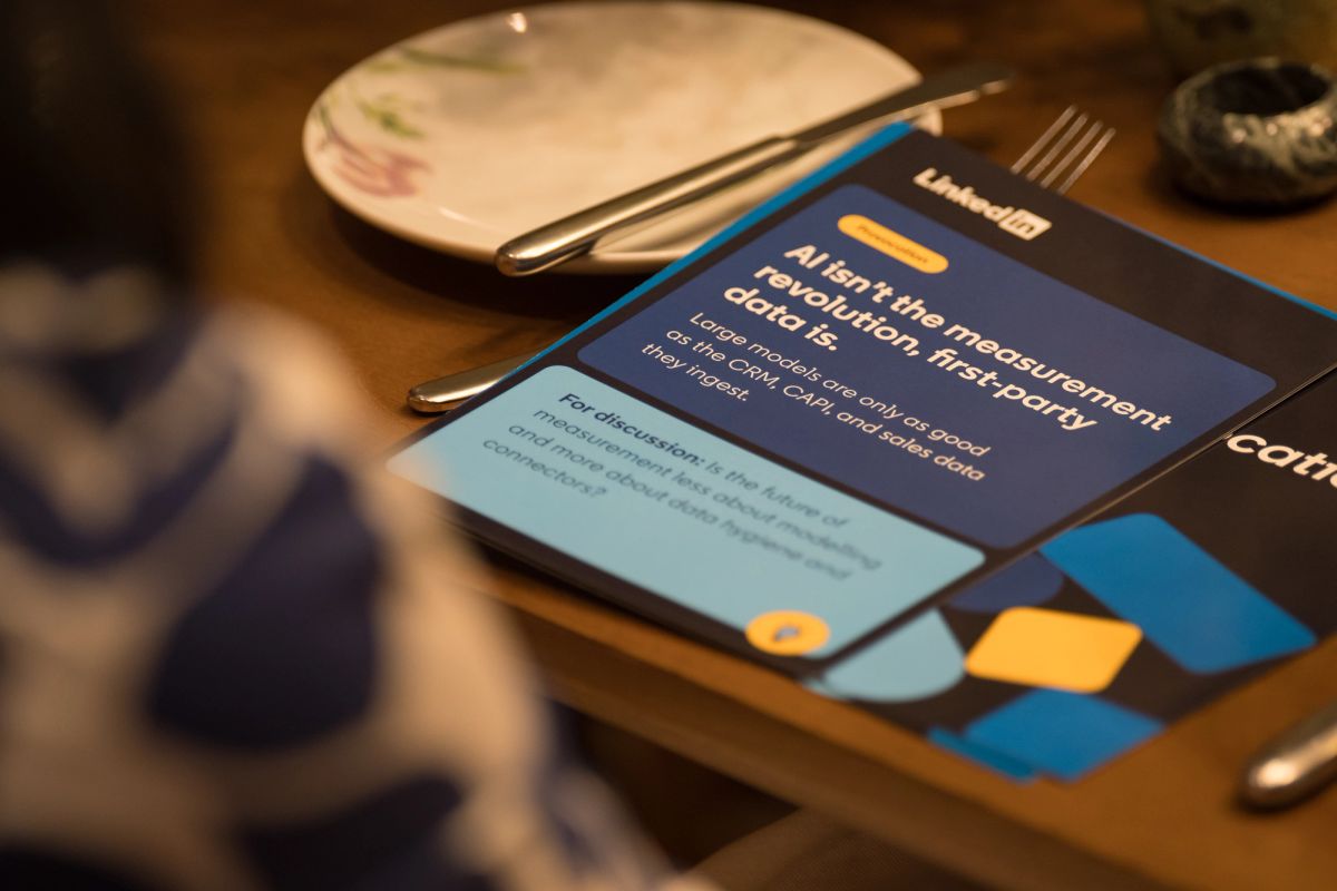 Tablet displaying presentation content sits on wooden table next to plate and utensils during panel discussion