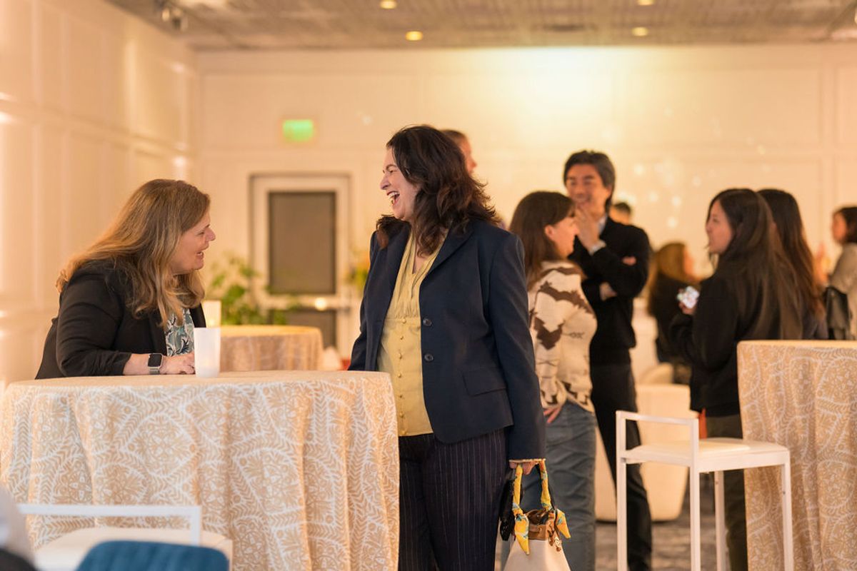 Professional women networking and conversing at cocktail tables during an indoor business reception event.