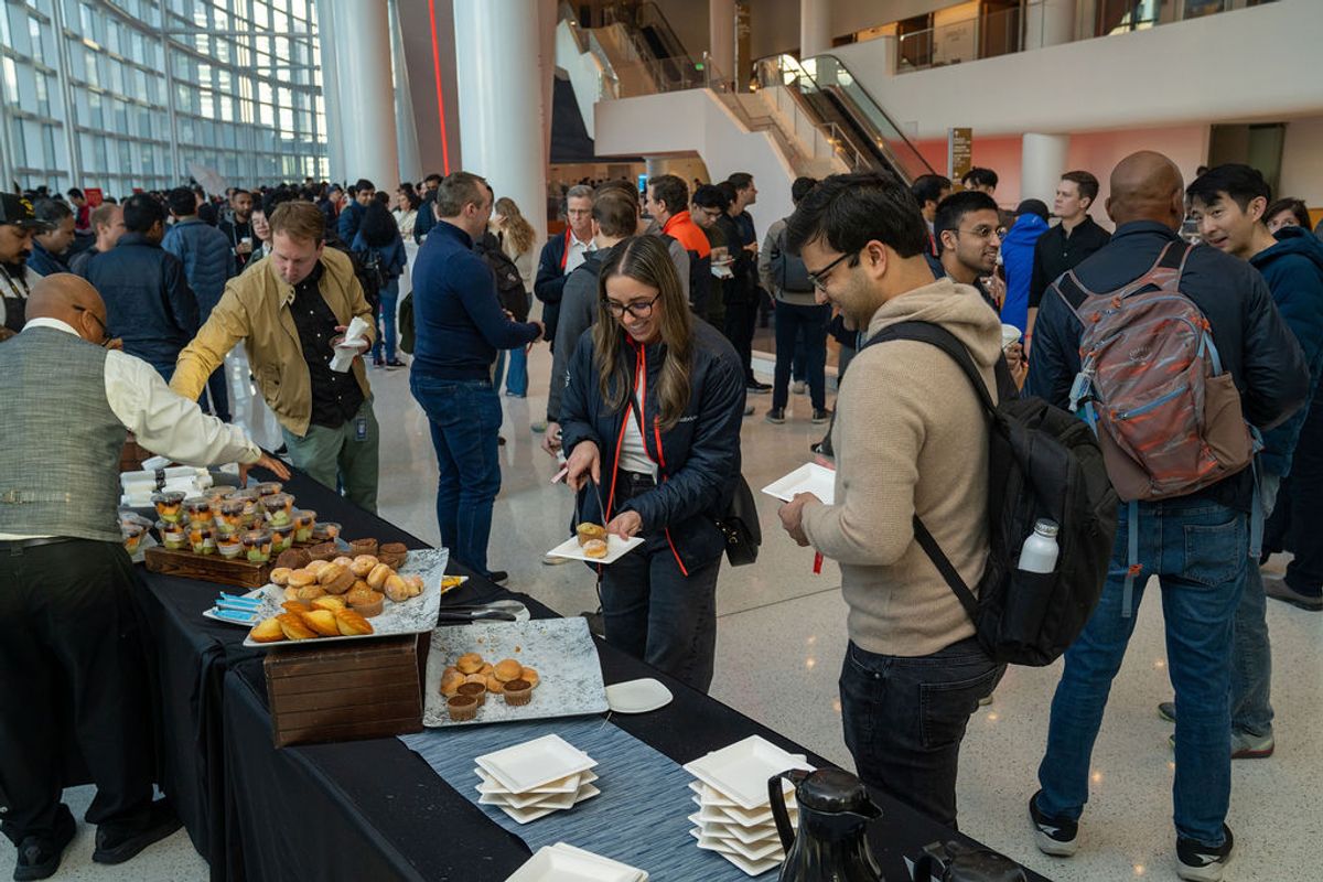 Conference attendees gather around a catering table with pastries and refreshments in a modern venue lobby