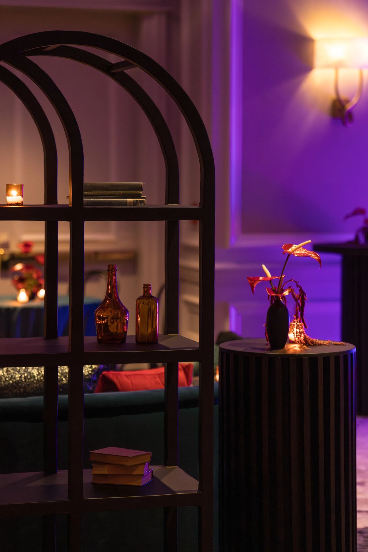 Modern lounge interior with purple ambient lighting, arched shelving unit displaying bottles and books, and.