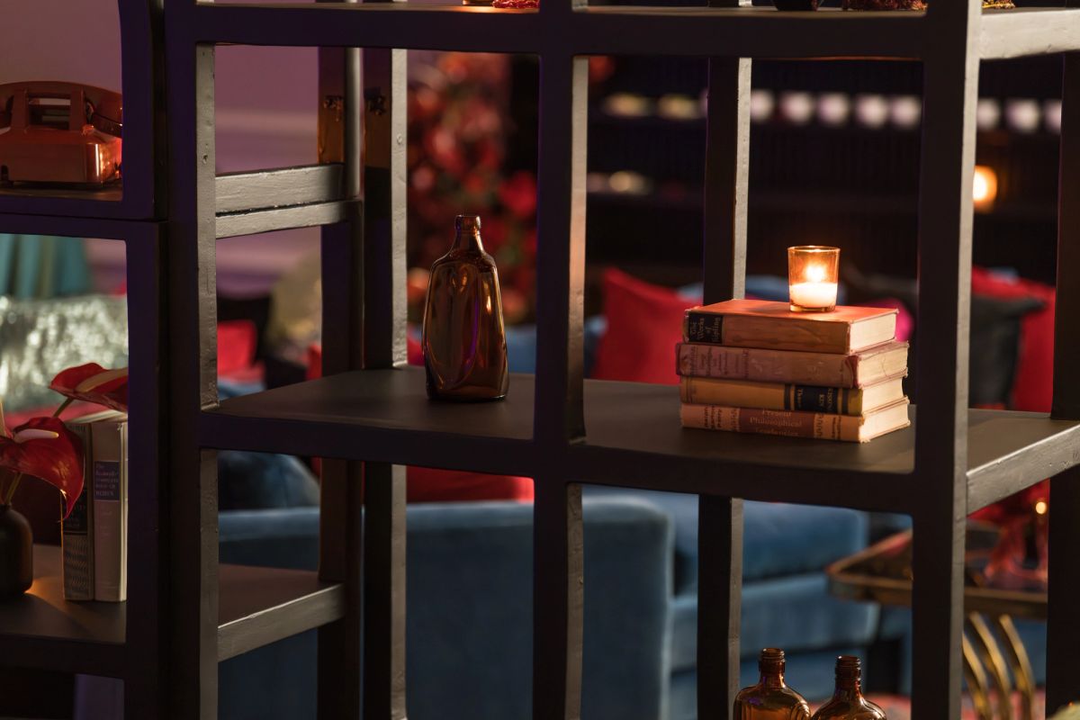 Dark wooden shelving unit with stacked books, a lit candle, brown bottles, and warm ambient lighting