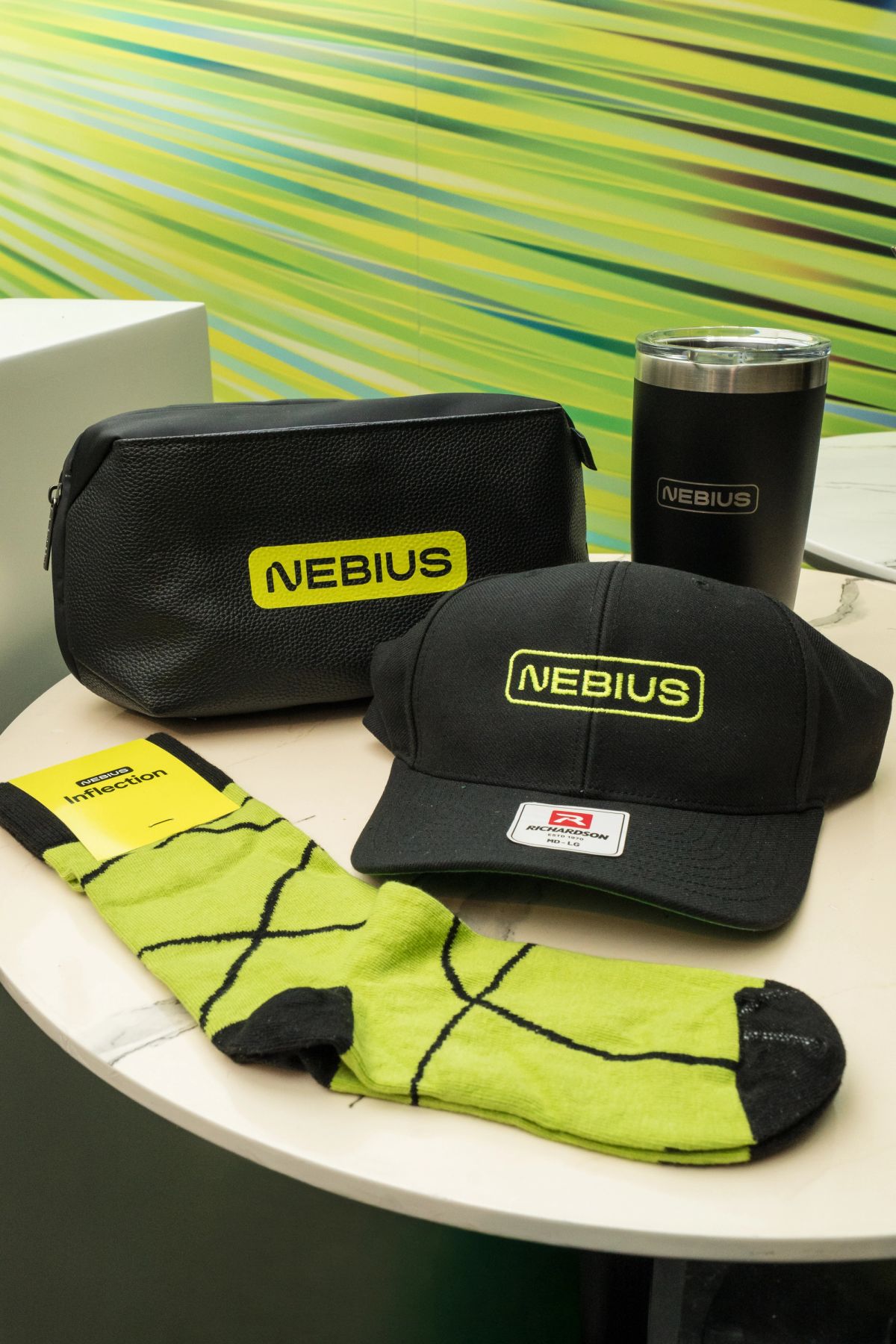 Nebius branded merchandise including cap, toiletry bag, tumbler, and neon green socks on a table.