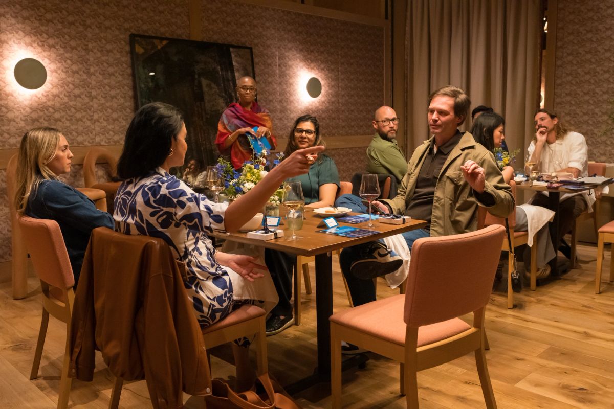 Panel discussion with speakers and attendees seated around tables in modern restaurant setting